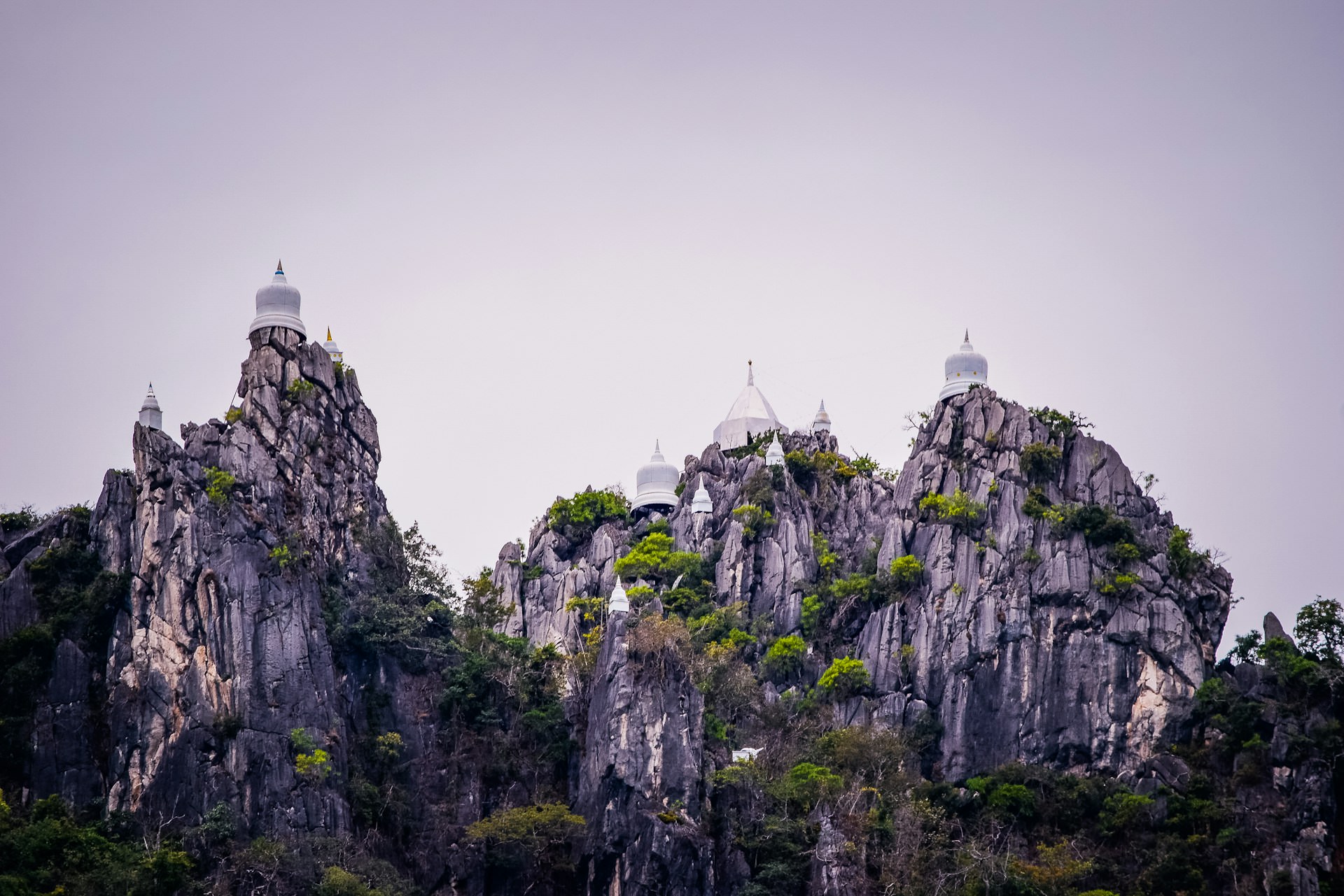 The striking Wat Chaloem Phra Kiat Phrachomklao Rachanusorn, featuring white pagodas perched on rocky peaks in Lampang, Thailand, surrounded by lush greenery and mountain views.