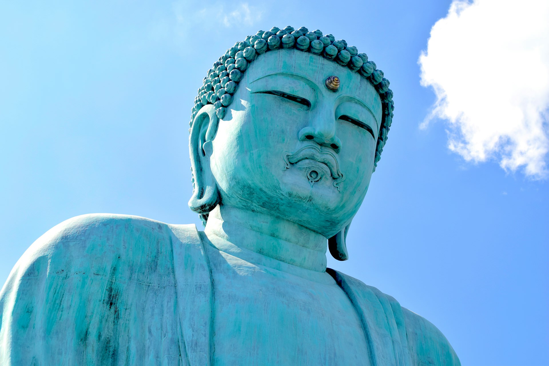 Close-up of the serene giant Buddha statue at Wat Prathat Doi Prachan Temple in Lampang, Thailand, against a bright blue sky.